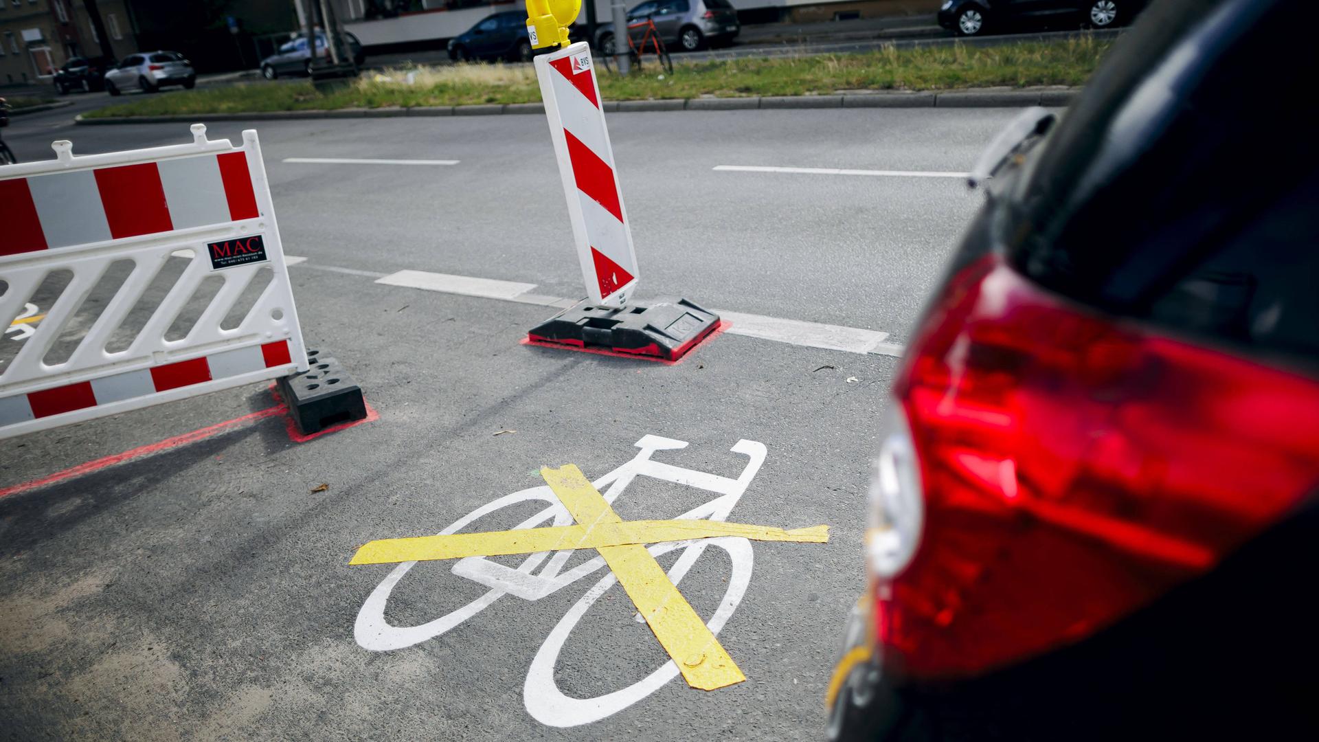 Das Piktogramm fuer einen neuen Radweg wurde mit einer gelben Markierung durchkreuzt. Daneben parkt ein Auto.