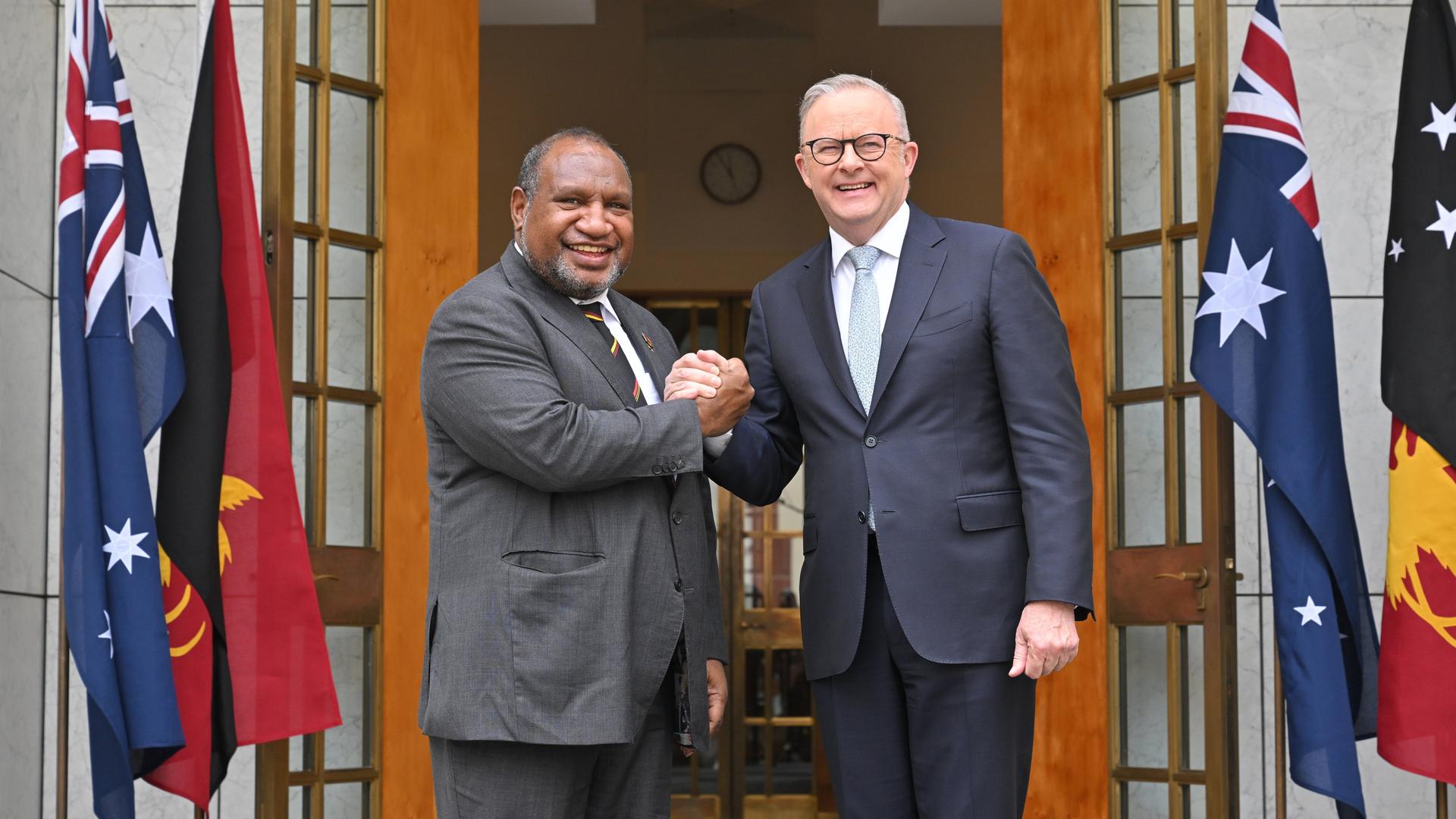 Australiens Premierminister Anthony Albanese (r.) und Papua-Neuguineas Premierminister James Marape posieren vor dem Eingang eines Gebäudes mit ineinandergelegten Händen und schauen in die Kamera