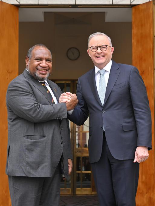 Australiens Premierminister Anthony Albanese (r.) und Papua-Neuguineas Premierminister James Marape posieren vor dem Eingang eines Gebäudes mit ineinandergelegten Händen und schauen in die Kamera