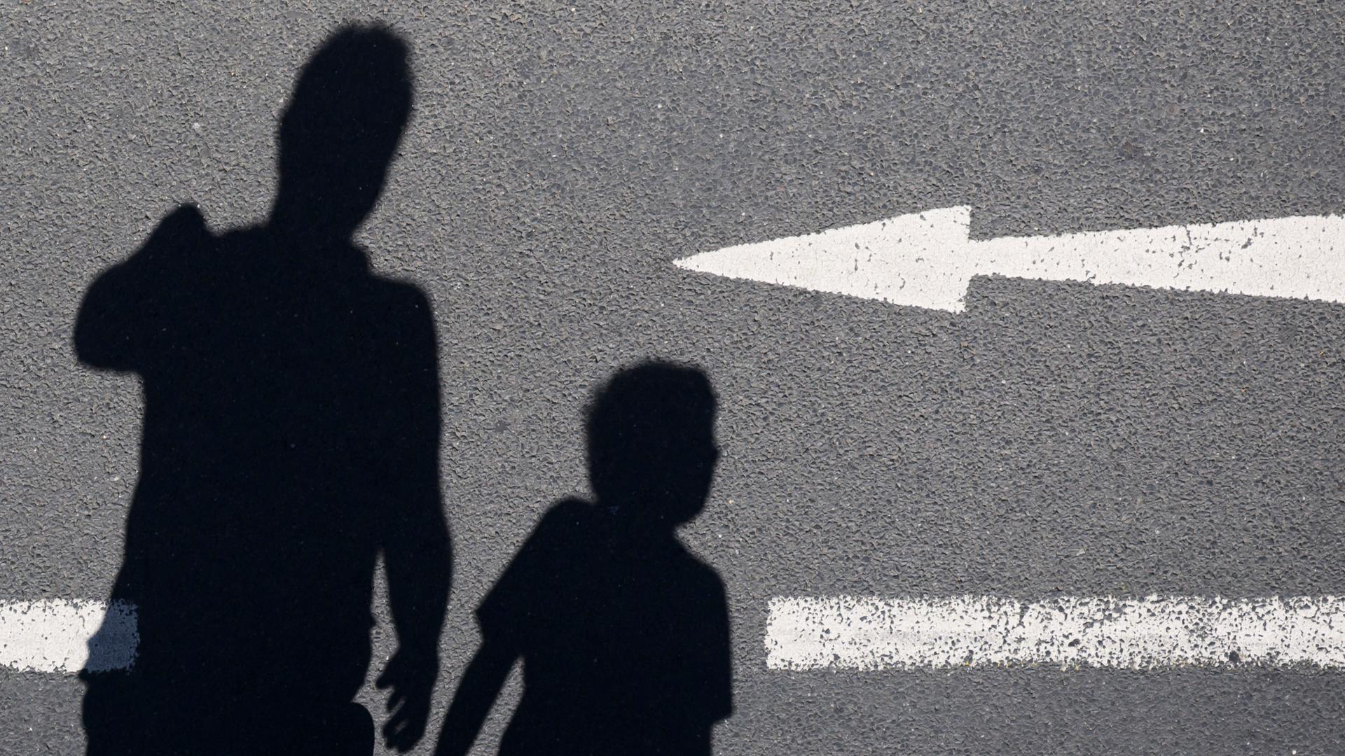 Der Schatten von einem Mann und einem Kind sind auf einer Straße mit einem Pfeil zu sehen. Der Schatten von einem Mann und einem Kind sind auf einer Straße mit einem Pfeil zu sehen.