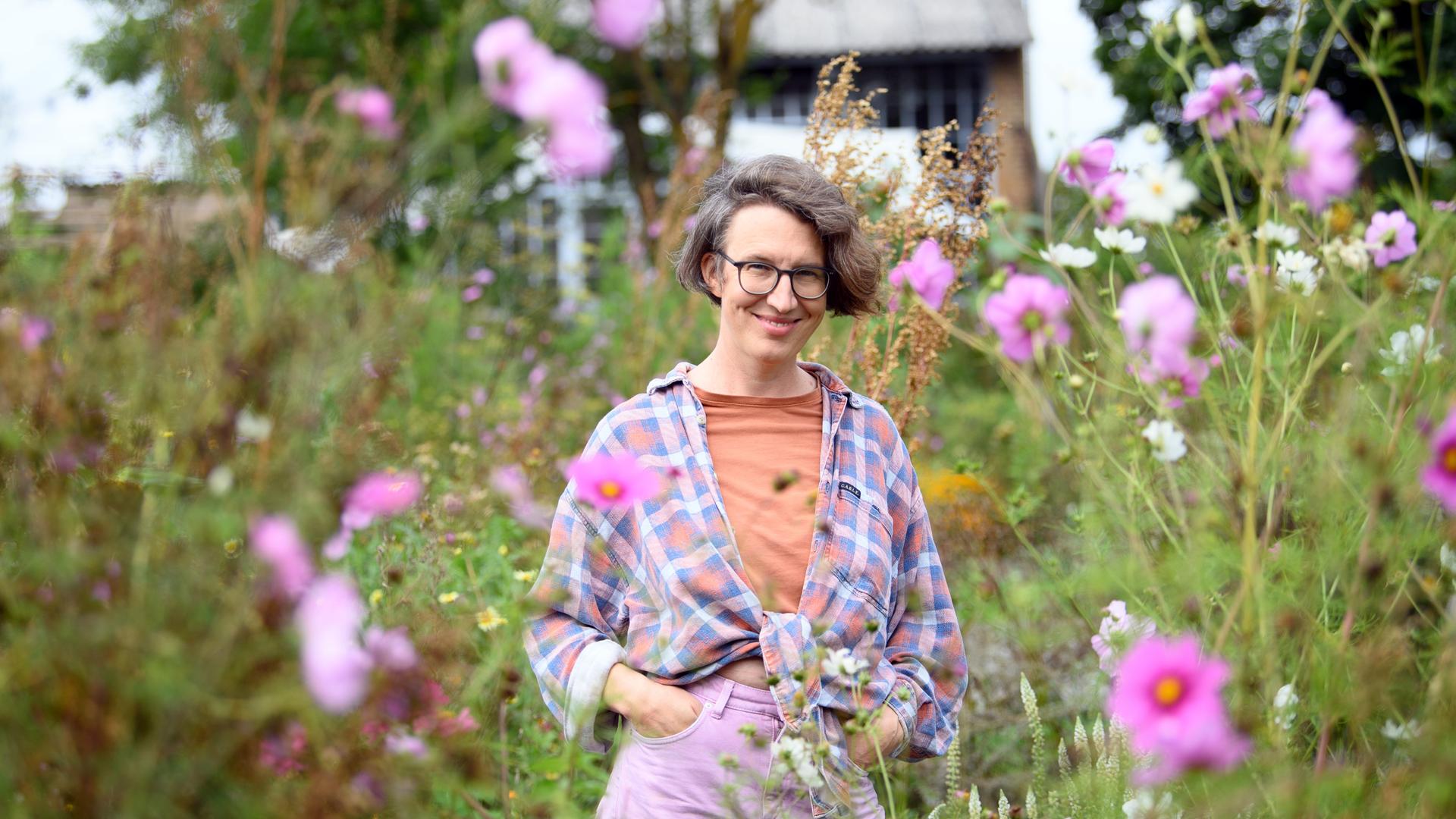 Die Filmemacherin Lola Randl steht in ihrem Garten zwischen Blumen, im Hintergrund ein Haus. 