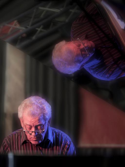 John Taylor sitzt im Jahr 2011 am Flügel und spielt, während er sich im Lack des aufgeklappten Instrumentes spiegelt. 