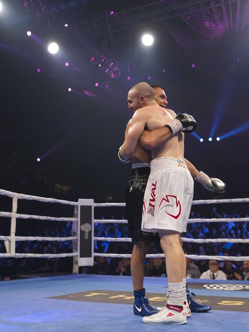 Zwei Boxer - Tim Tszyu and Joel Camilleri - stehen in einem Boxring nach einem Kampf und umarmen sich. Neben ihnen steht ein Ringrichter.