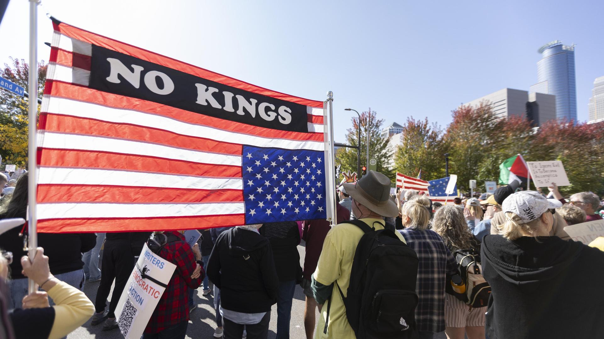 Demonstranten im Commons Park in Minneapolis, Minnesota zum "No Kings!"-Protest, sie tragen eine US-amerikanische Fahne mit der Aufschrift "No Kings"