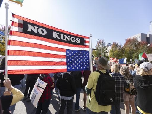Demonstranten im Commons Park in Minneapolis, Minnesota zum "No Kings!"-Protest, sie tragen eine US-amerikanische Fahne mit der Aufschrift "No Kings"