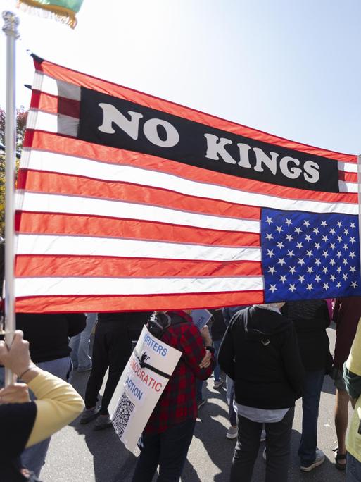 Demonstranten im Commons Park in Minneapolis, Minnesota zum "No Kings!"-Protest, sie tragen eine US-amerikanische Fahne mit der Aufschrift "No Kings"
