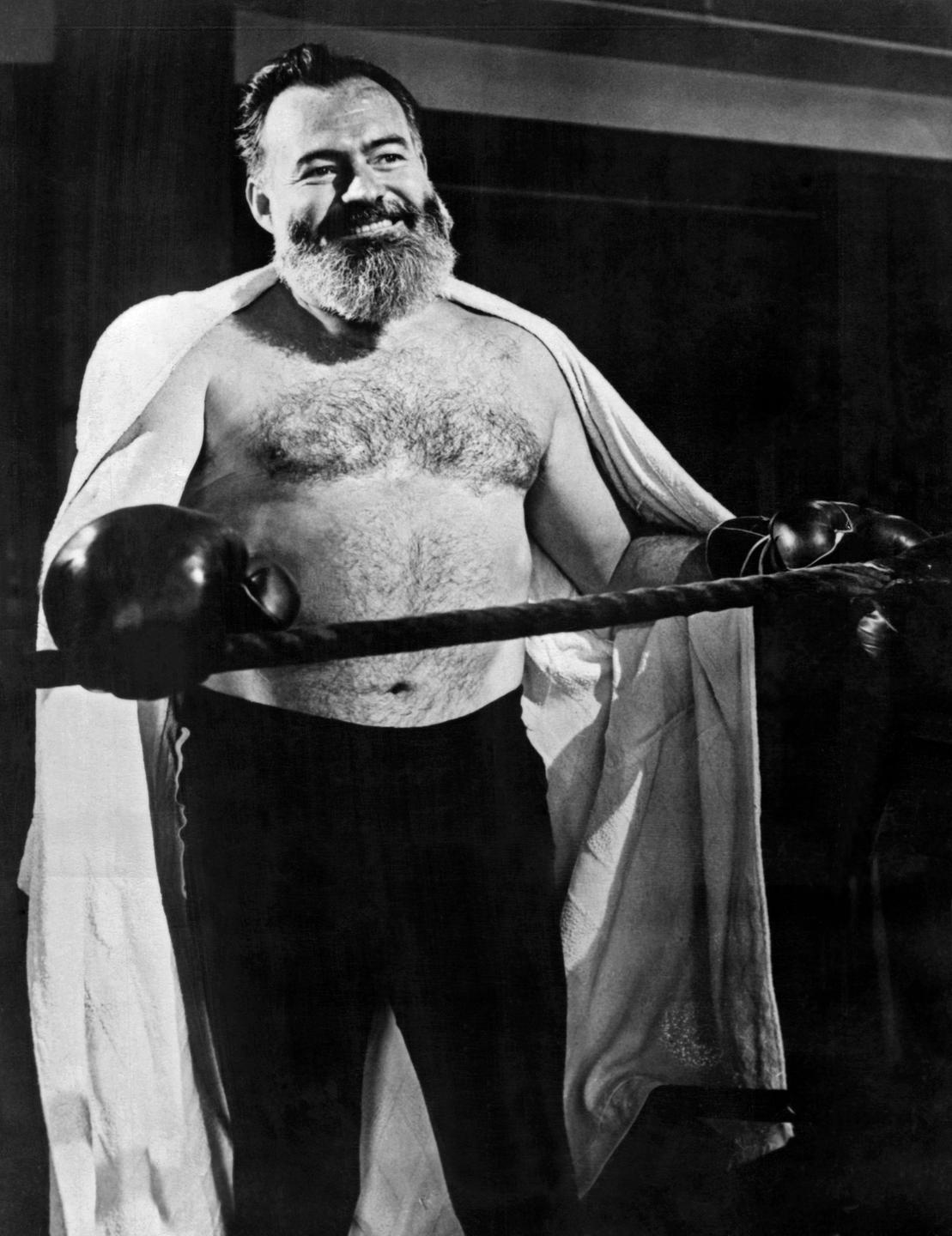 Ein Mann mittleren Alters mit Vollbart steht in einem Boxring mit nacktem Oberkörper, Handtuch über den Schultern und Boxhandschuhen.