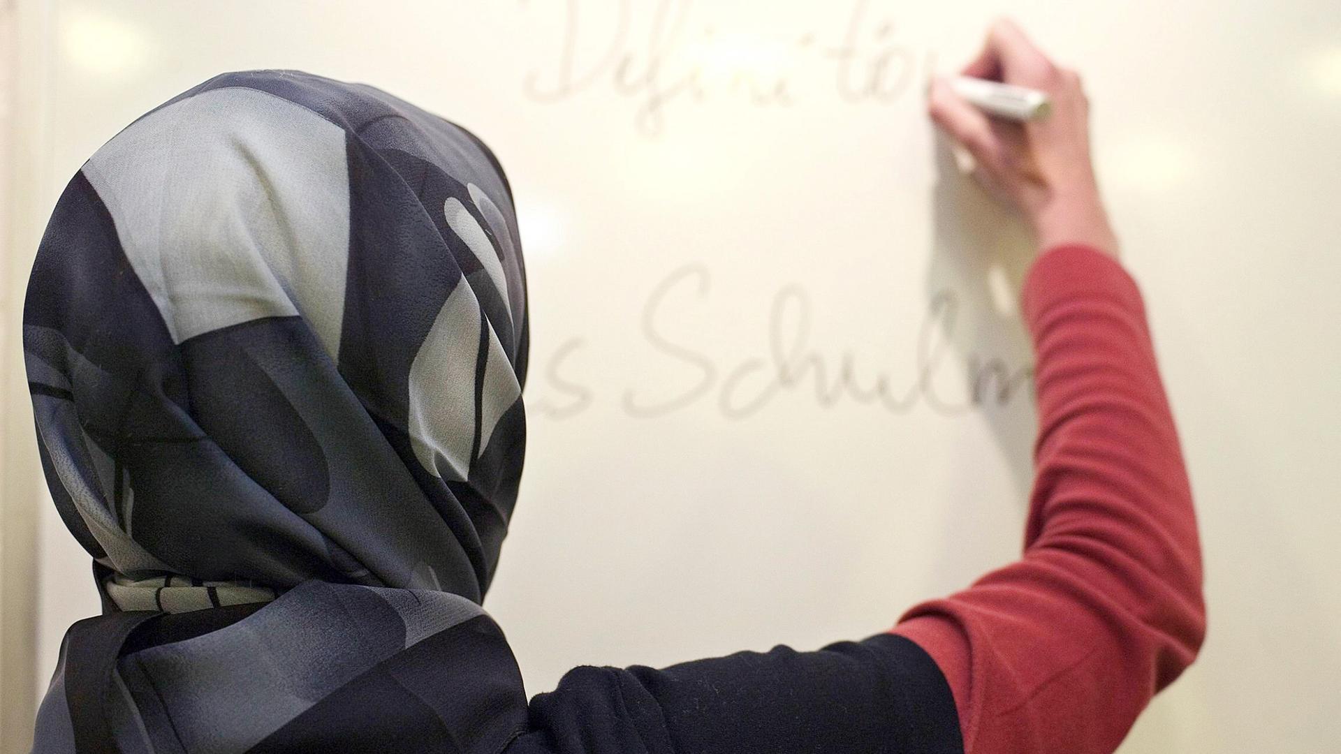 Eine Lehrerin mit Kopftuch in einer deutschen Schule schreibt an eine Tafel.