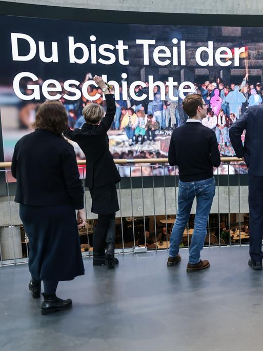 Der neue Slogan „Du bist Teil der Geschichte“ ist im Haus der Geschichte auf einer Videowand zu sehen, davor stehen Menschen. Das Haus der Geschichte in Bonn eröffnet seine neu gestaltete Dauerausstellung.
