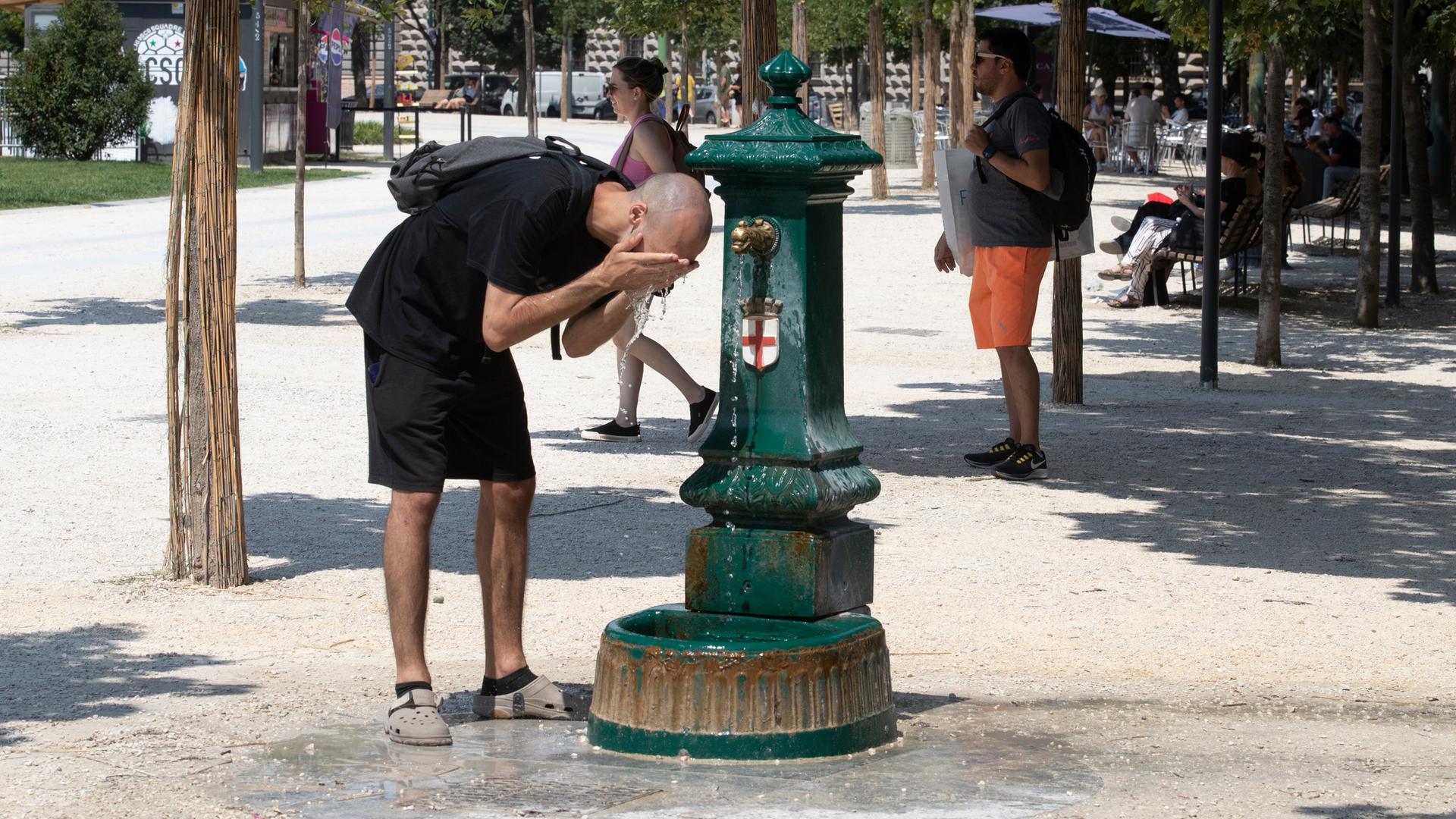 Ein Mann steht gebückt vor einem Trinkbrunnen und erfrischt sich mit dem kalten Wasser. 