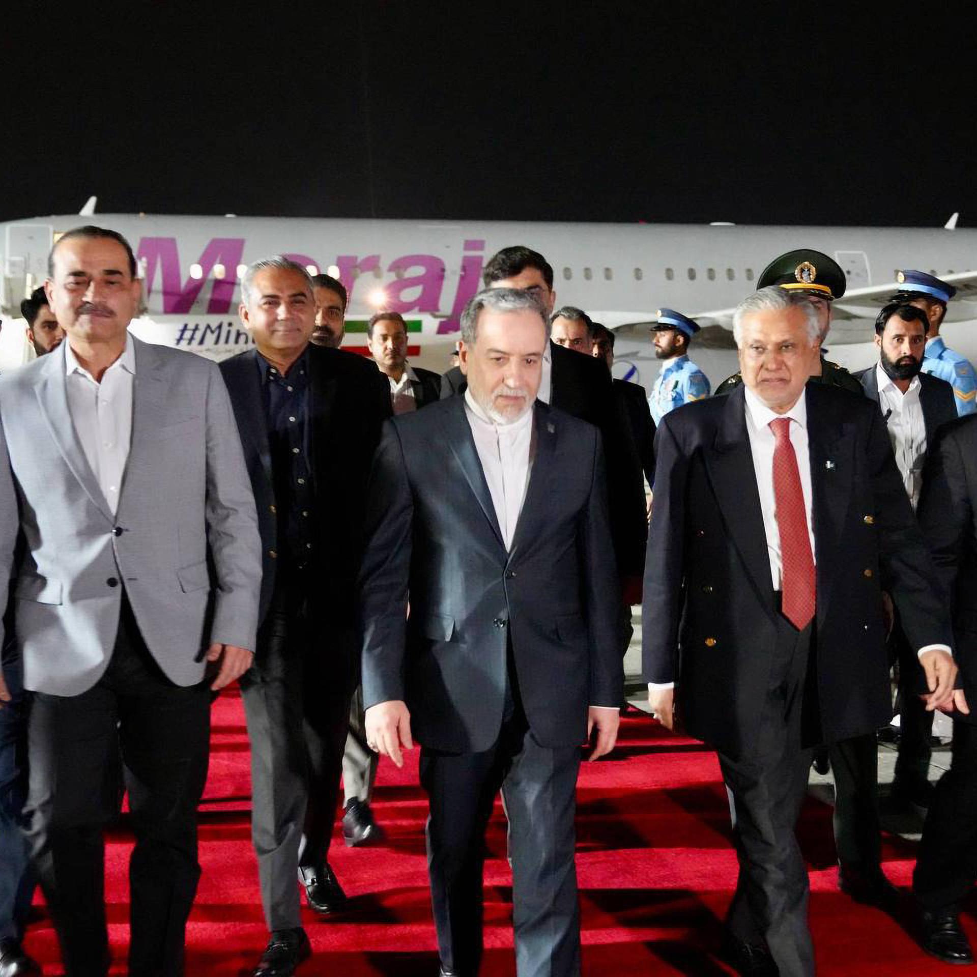 Mehrere Männer laufen über einen roten Teppich auf einem Rollfeld eines Flughafens. Es ist Nacht.