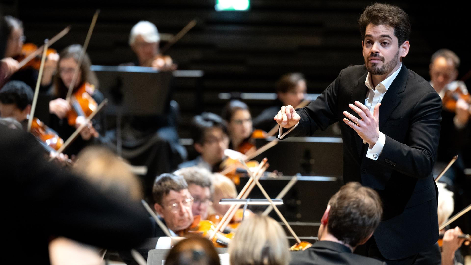 Lahav Shani dirigiert mit zugewandte Geste die Münchner Philharmoniker. Lahav Shani dirigiert mit zugewandte Geste die Münchner Philharmoniker.