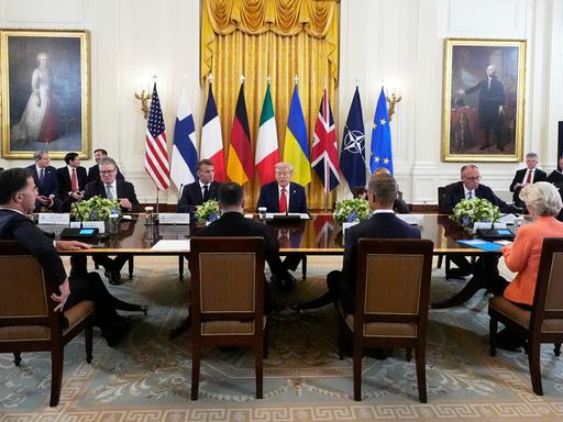 Donald Trump sitzt an einem Tisch mit dem britischen Premier Keir Starmer, Frankreichs Präsident Emmanuel Macron, Bundeskanzler Friedrich Merz, Ukraines Präsident Wolodymyr Selenskyj und EU-Kommissionspräsidentin Ursula von der Leyen