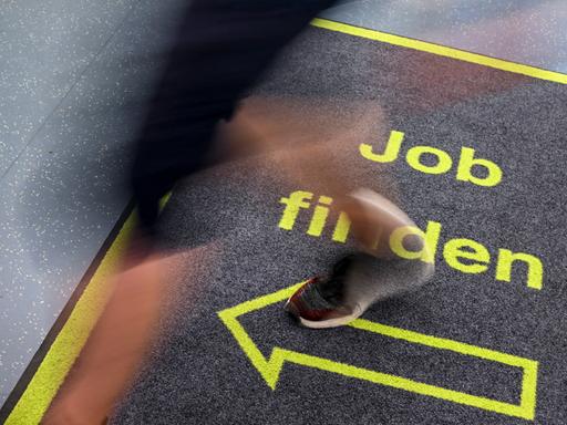 Ein Mann geht in einem Jobcenter über einen Teppich mit der Aufschrift "Job finden".