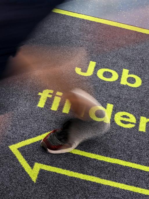 Ein Mann geht in einem Jobcenter über einen Teppich mit der Aufschrift "Job finden".