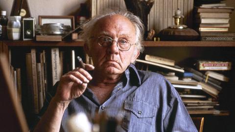 Der Berliner Maler und Grafiker Arno Mohr sitzt im Jahr 1978 mit einer Zigarre in der Hand vor einer Regalwand in seiner Wohnung in Berlin.