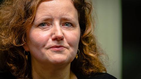 Nahaufnahme einer Frau mit roten Locken und blauen Augen, die nachdenklich in die Kamera schaut.