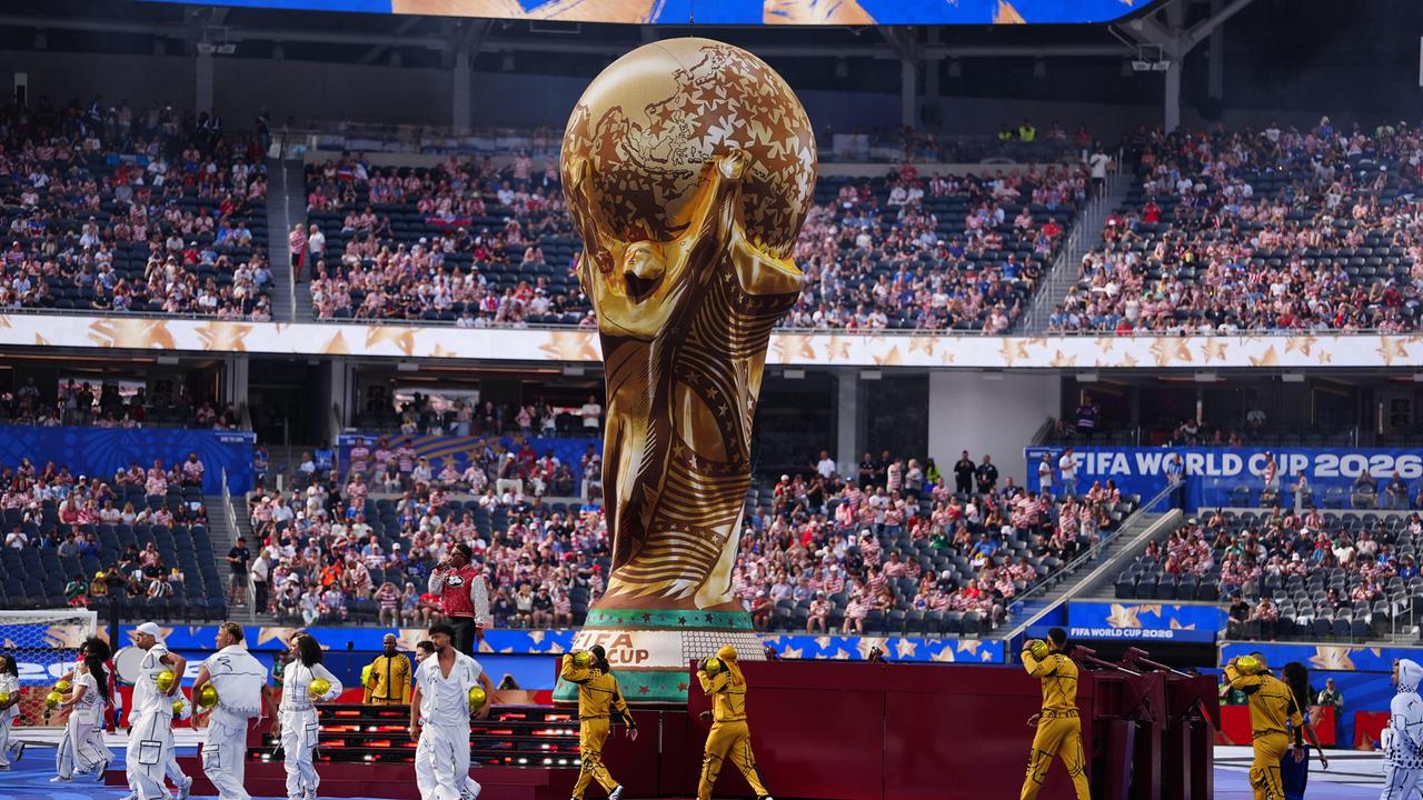 Die Fußball-Weltmeisterschaften 2026 finden in mehreren Ländern statt. Ein riesiger Pokal ist auf dem Spielfeld, viele Menschen sitzen im Publikum und feiern auf dem Platz. 