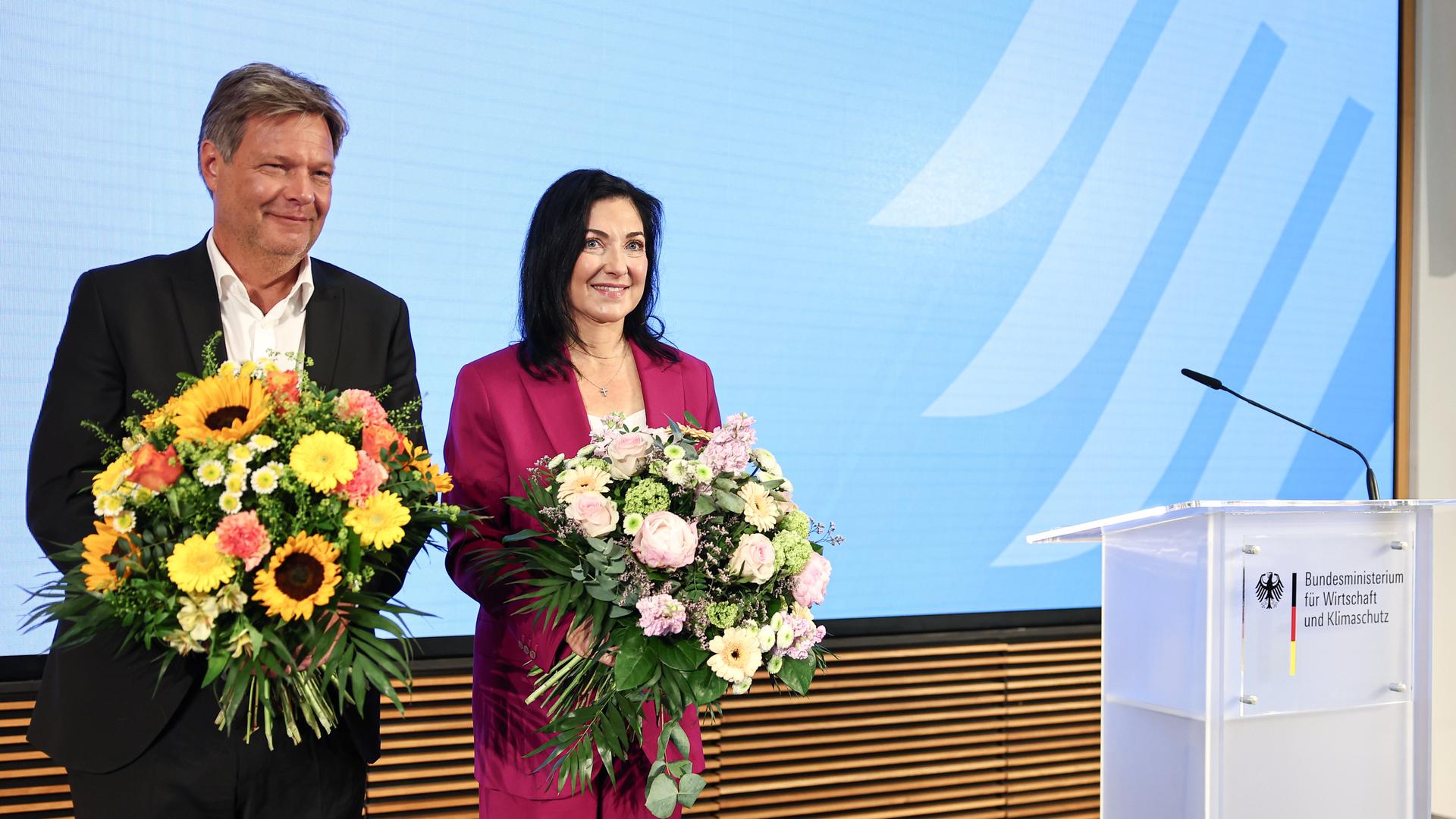 Robert Habeck (l, Bündnis 90/Die Grünen), ehemaliger Vizekanzler und Bundesminister für Wirtschaft und Klimaschutz, und Katherina Reiche (CDU), Bundesministerin für Wirtschaft und Energie, stehen mit Blumen auf der Bühne im Bundeswirtschaftsministerium. Robert Habeck (l, Bündnis 90/Die Grünen), ehemaliger Vizekanzler und Bundesminister für Wirtschaft und Klimaschutz, und Katherina Reiche (CDU), Bundesministerin für Wirtschaft und Energie, stehen mit Blumen auf der Bühne im Bundeswirtschaftsministerium.