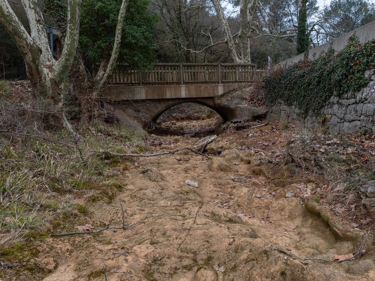 Eine Brücke führt über ein ausgetrocknetes Flussbett. 