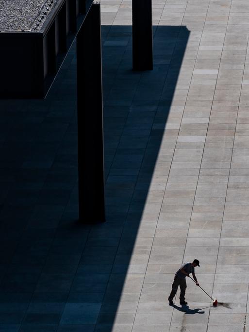 Ein Mann fegt den grauen Boden vor dem Gebäude der Neuen Nationalgalerie in Berlin.