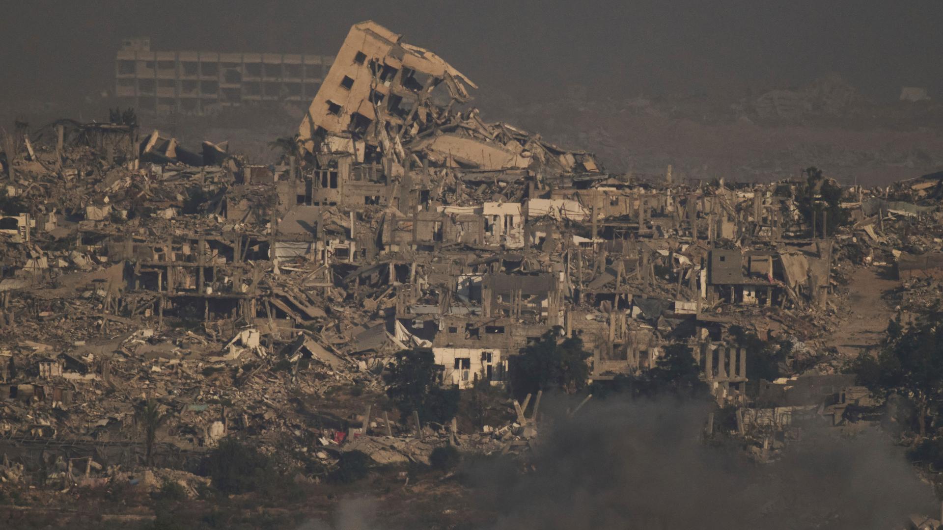 Ein Gebiet im Gazastreifen. Zu sehen sind zerstöre Häuser, Rauch steigt auf.