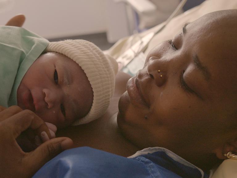 Eine Frau liegt mit ihrem Neugeborenen auf der Brust im Bett