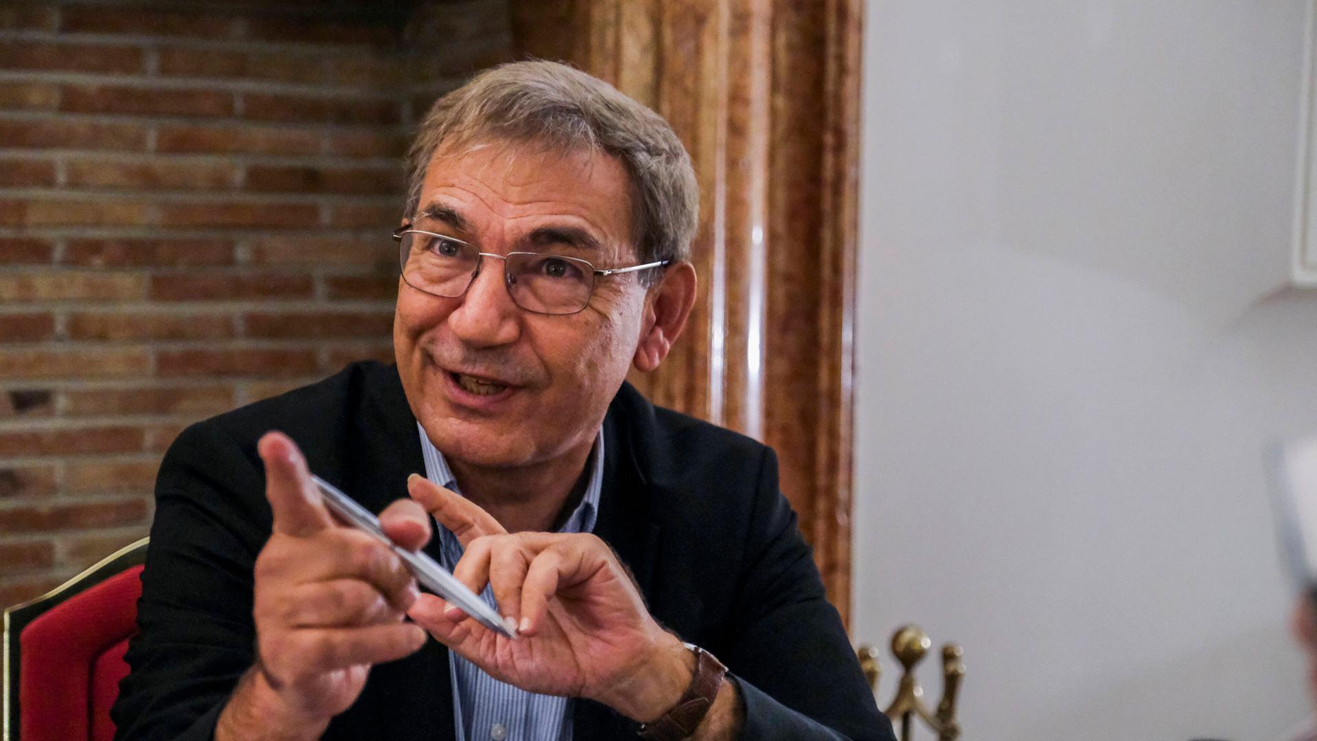 Der türkische Schriftsteller Orhan Pamuk sitzt an einem Tisch und zeigt mit einem Zeigefinger nach vorn.