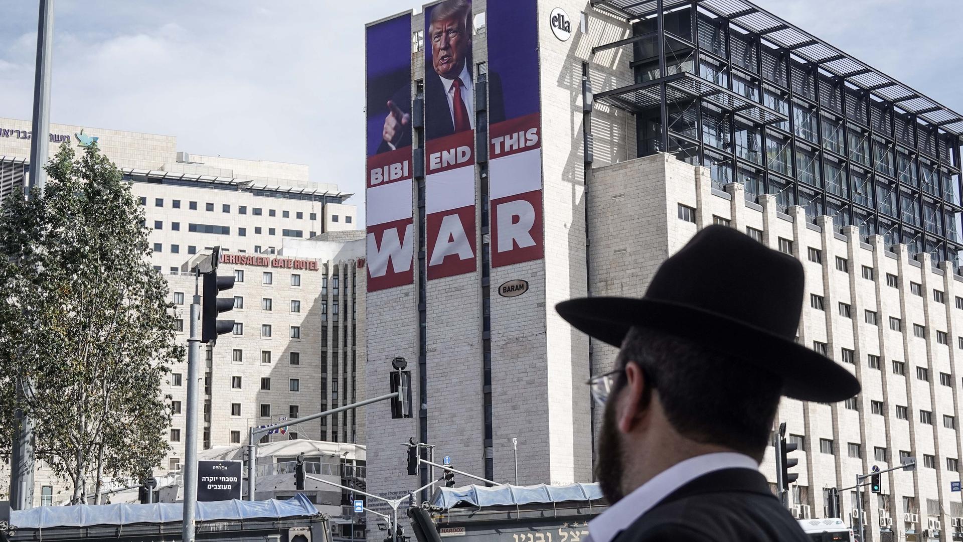 Ein orthodoxer Jude schaut auf ein Plakat das Donald Trump und die Worte "Bibi End This War" zeigt.