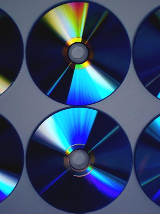 Auf dem Bild sind sechs CDs zu sehen, nicht mit der Cover-Seite, sondern die mit Inhalt bespielte Seite. Die CD-Ringe glänzen in blauen und gelben Farben.