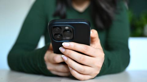 Hände einer jungen Frau umgreifen ein Smartphone an einem Tisch. Hände einer jungen Frau umgreifen ein Smartphone an einem Tisch.