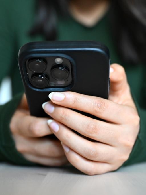 Hände einer jungen Frau umgreifen ein Smartphone an einem Tisch.