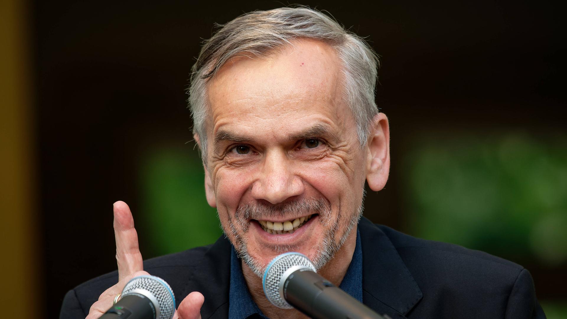 Lutz Seiler sitzt mit erhobenem Zeigefinger lachend vor einem Mikrofon.
