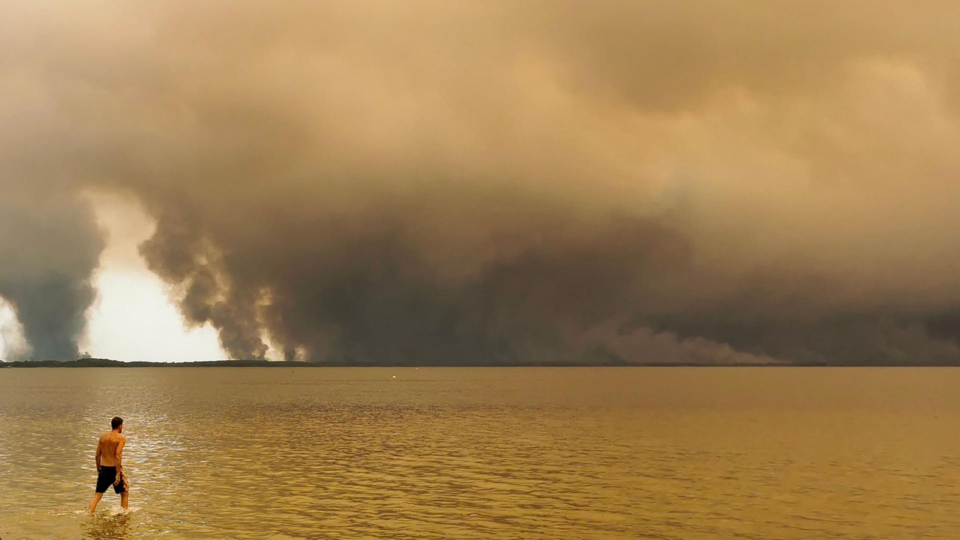 Das Foto zeigt einen Strandbesucher. Er spaziert am Strand von Moutchic in Lacanau im Südwesten Frankreichs am Etang de Lacanau entlang, während Rauchwolken von einem Waldbrand in den Himmel aufsteigen. Das Foto zeigt einen Strandbesucher. Er spaziert am Strand von Moutchic in Lacanau im Südwesten Frankreichs am Etang de Lacanau entlang, während Rauchwolken von einem Waldbrand in den Himmel aufsteigen.
