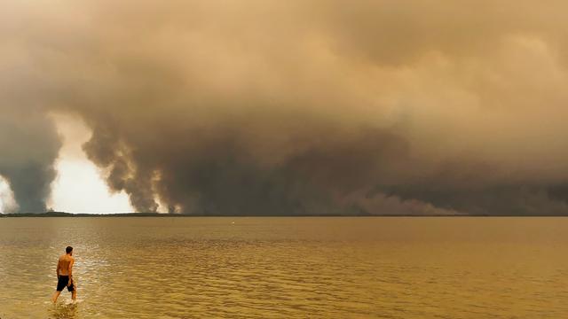 Das Foto zeigt einen Strandbesucher. Er spaziert am Strand von Moutchic in Lacanau im Südwesten Frankreichs am Etang de Lacanau entlang, während Rauchwolken von einem Waldbrand in den Himmel aufsteigen.