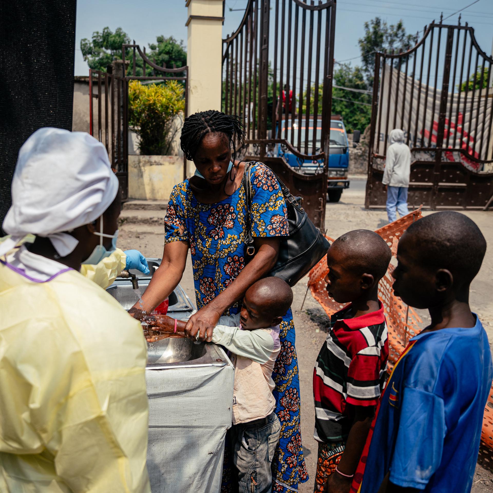 Eine Mutter hilft ihren Kindern, sich an einer Kontrollstelle die Hände zu waschen, bevor sie das Kyeshero-Krankenhaus in Goma betreten.