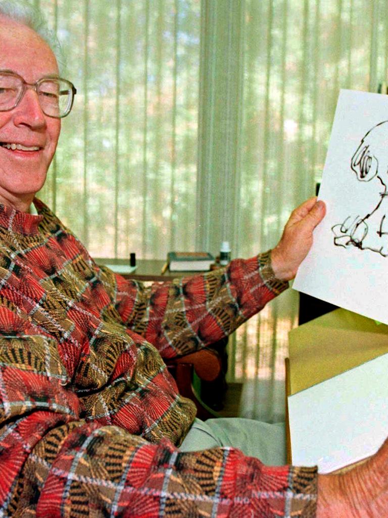 Charles Schulz hält eine Zeichnung von Snoopy in der Hand und lächelt.