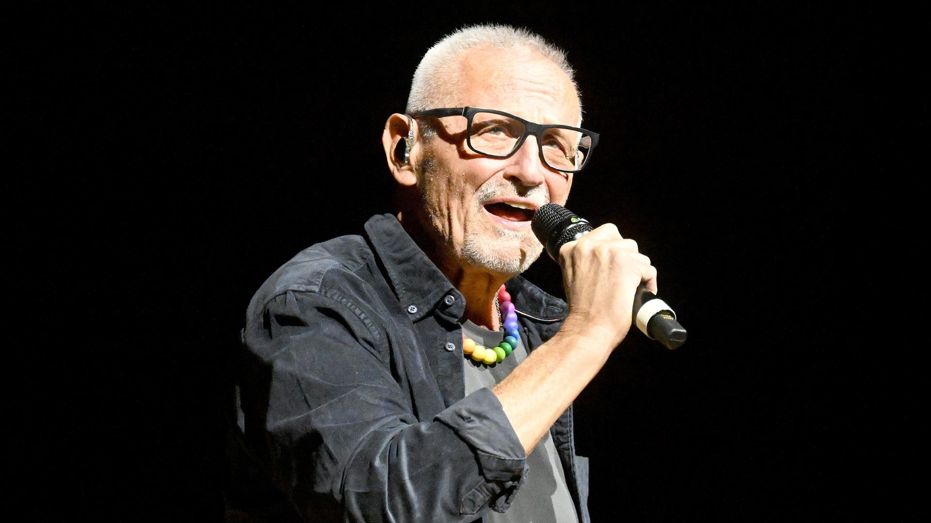 Der Liedermacher Konstantin Wecker steht auf einer Bühne und singt in ein Mikrofon.