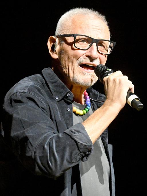 Der Liedermacher Konstantin Wecker steht auf einer Bühne und singt in ein Mikrofon.