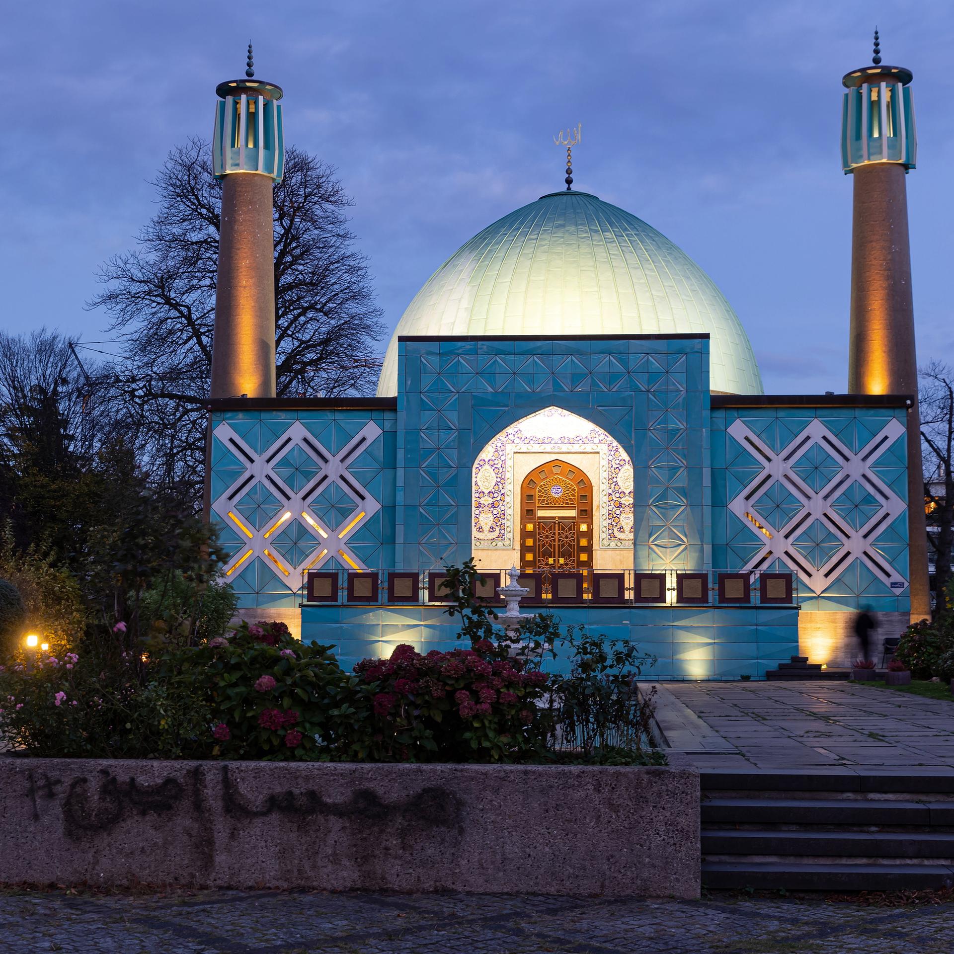 Blick auf das Islamische Zentrum Hamburg (IZH) der Imam-Ali-Moschee am frühen Abend. Das Gebäude hat ein hohes, großes Kuppeldach. Rechts und links stehen zwei Minarette. 