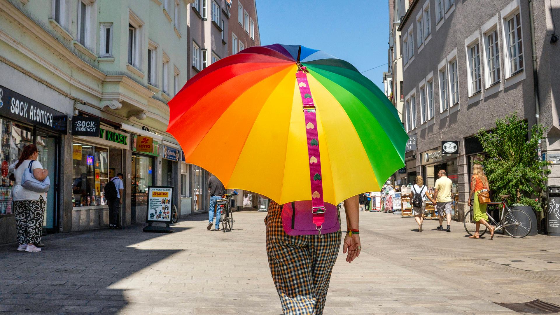 Eine Frau geht bei 35 Grad mit Regenbogen-Sonnenschirm durch die Augsburger Fußgängerzone.