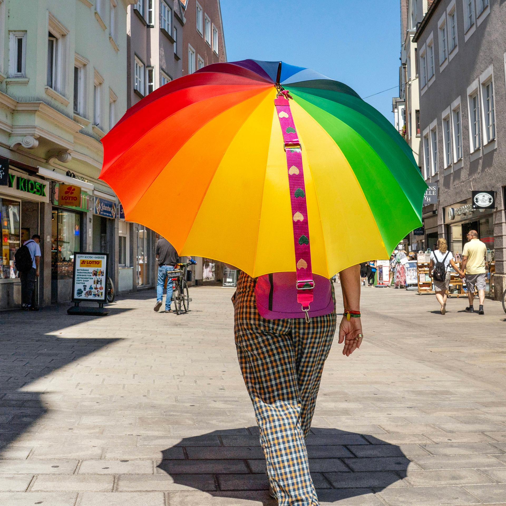 Eine Frau geht bei 35 Grad mit Regenbogen-Sonnenschirm durch die Augsburger Fußgängerzone.