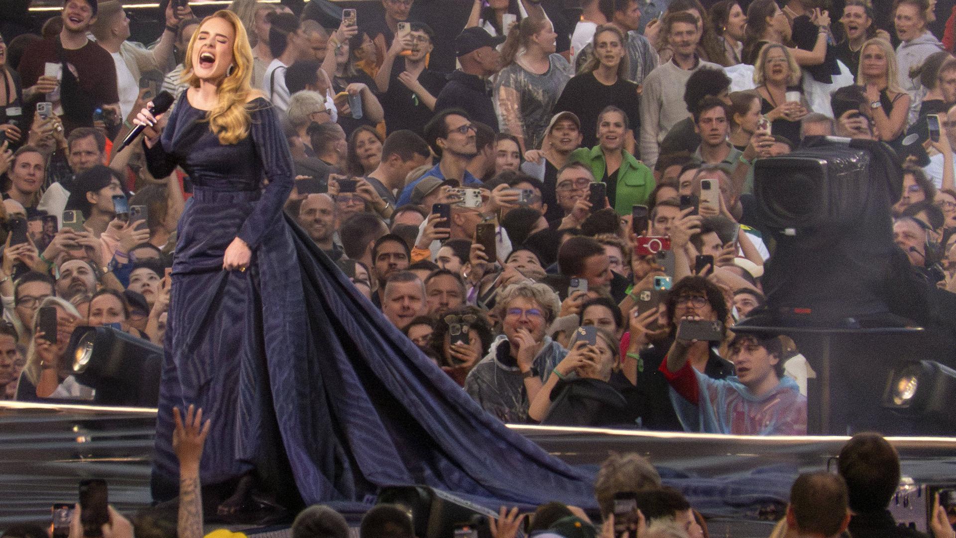 Adele während des ersten Konzerts in München: Sie steht in einem langen schwarzen Kleid auf der Bühne und singt. Im Hintergrund jubeln Fans. Adele während des ersten Konzerts in München: Sie steht in einem langen schwarzen Kleid auf der Bühne und singt. Im Hintergrund jubeln Fans.