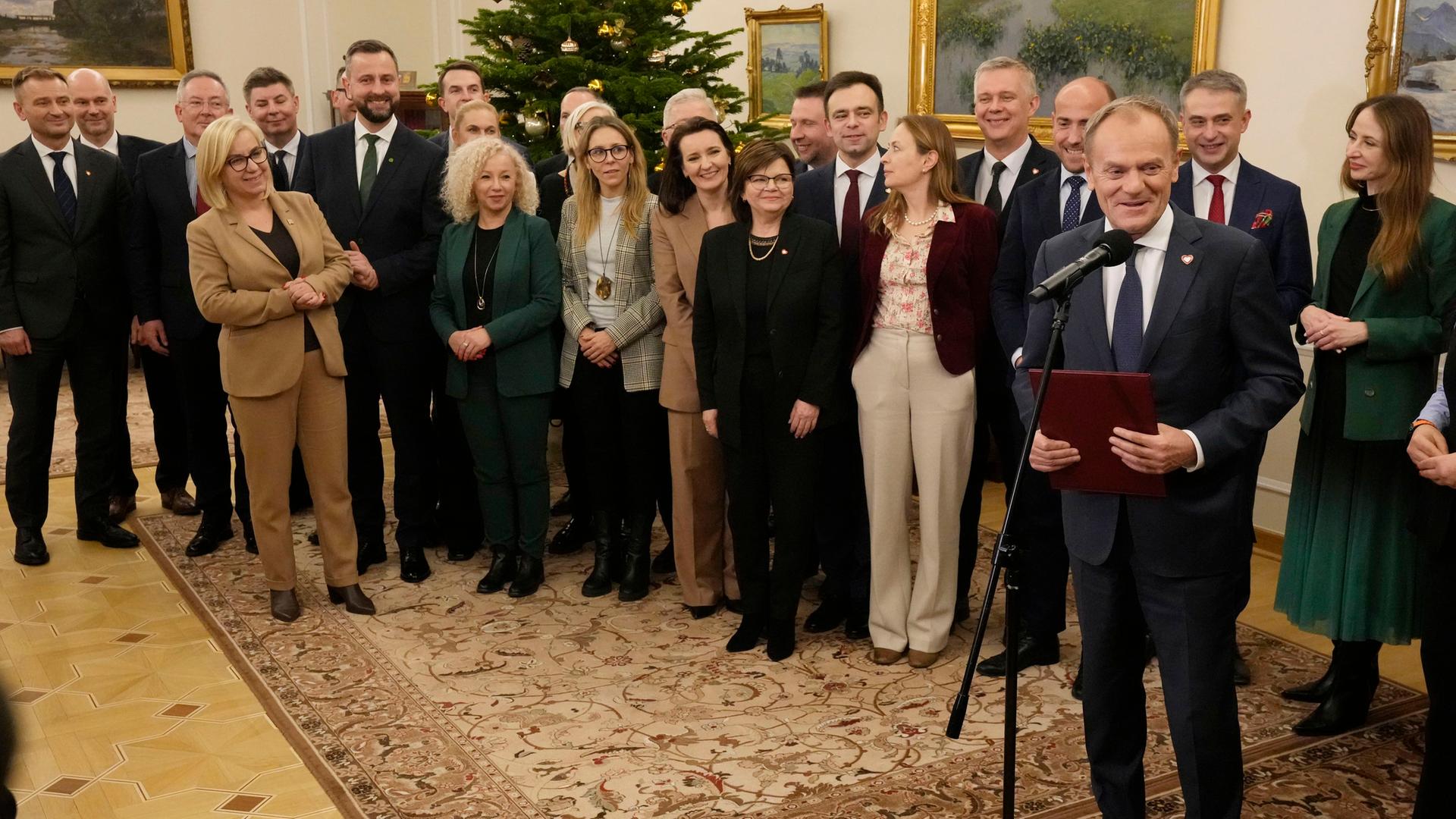 Donald Tusk und sein neues Kabinett stehen nach ihrer Vereidigung im Halbkreis. Tusk steht vor einem Mikrofon.