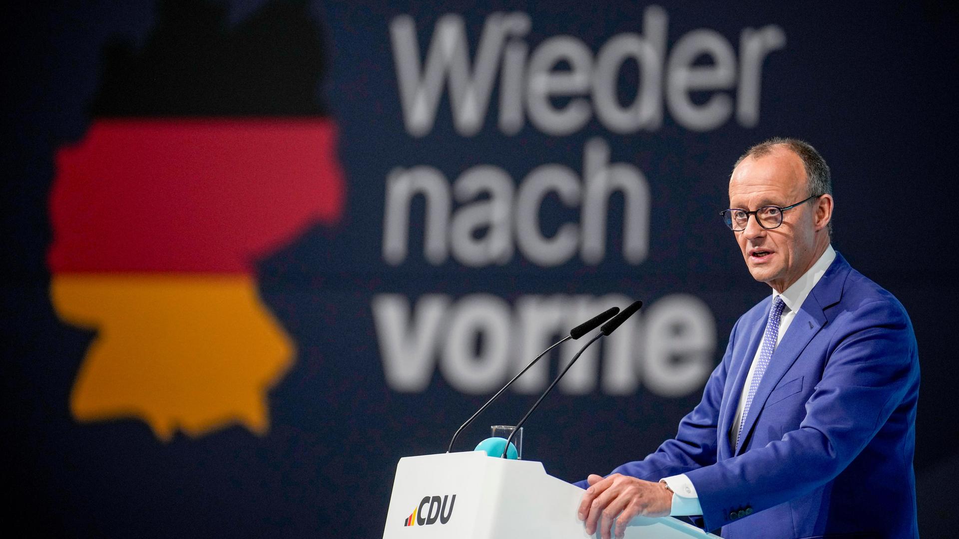 Friedrich Merz, CDU-Kanzlerkandidat ist auf zwei großen Bildschirmen zu sehen. Davor sitzen die Delegierten.