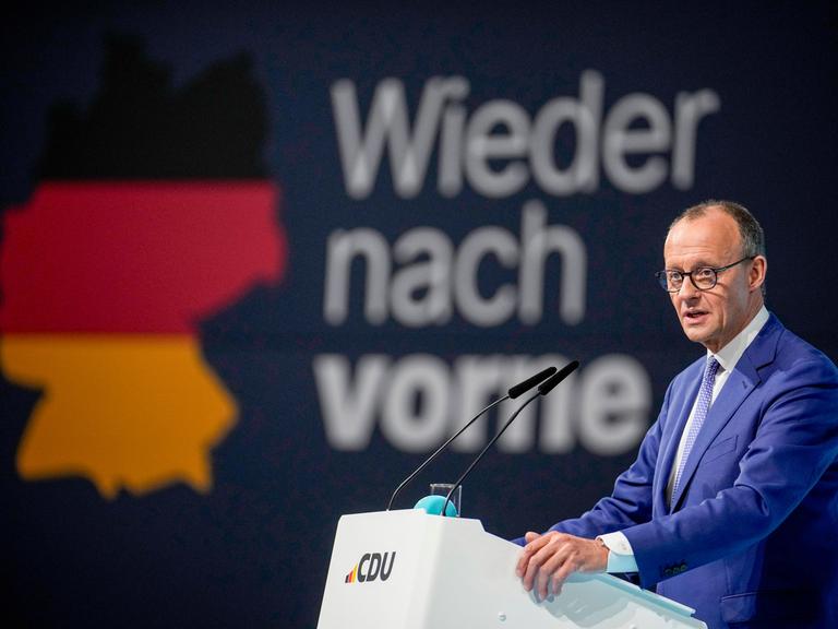 Friedrich Merz, CDU-Kanzlerkandidat ist auf zwei großen Bildschirmen zu sehen. Davor sitzen die Delegierten.