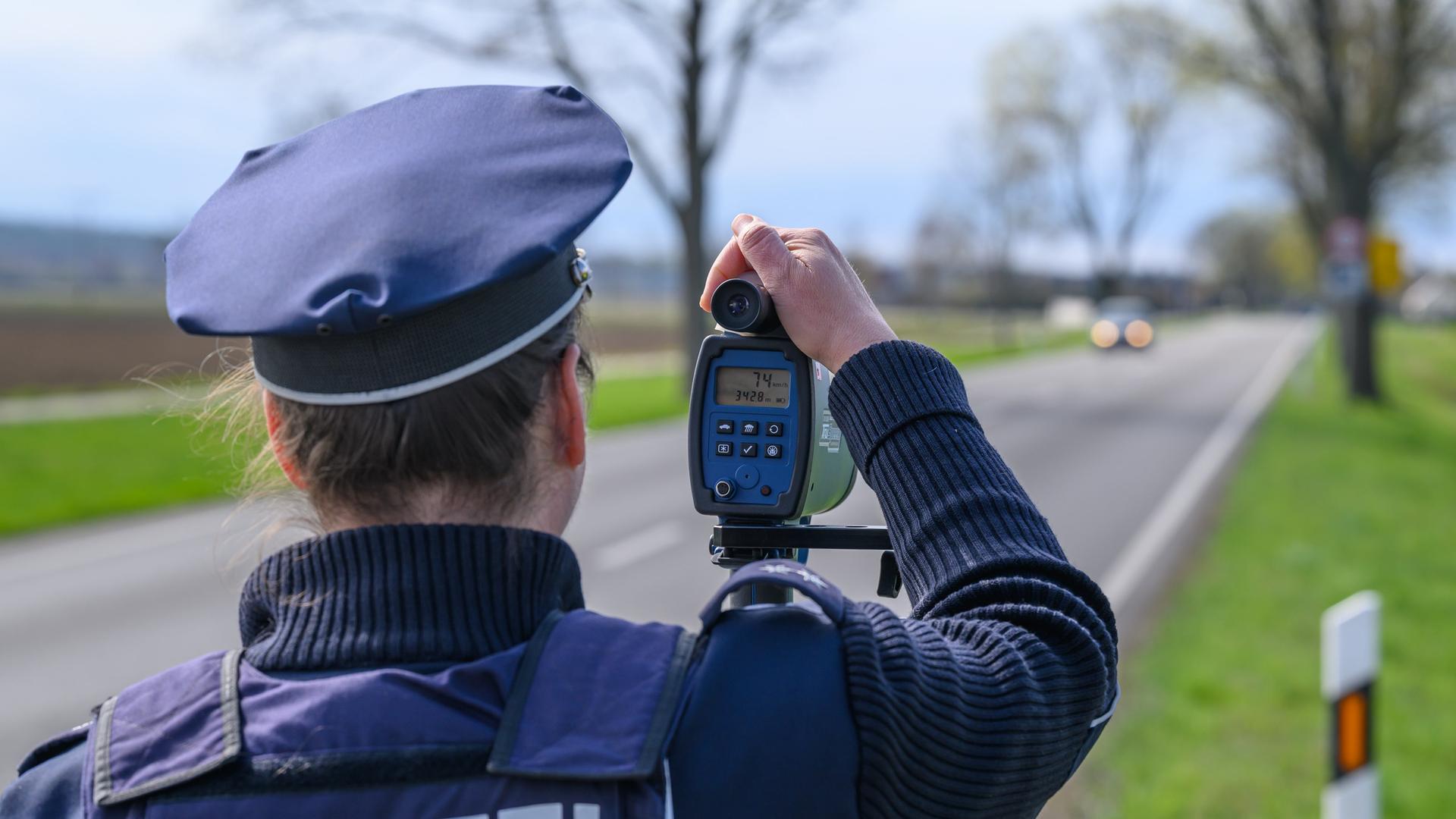Eine Polizeibeamtin steht mit einem Lasermessgerät an einer Bundesstraße und überwacht die Geschwindigkeit der Fahrzeuge. 