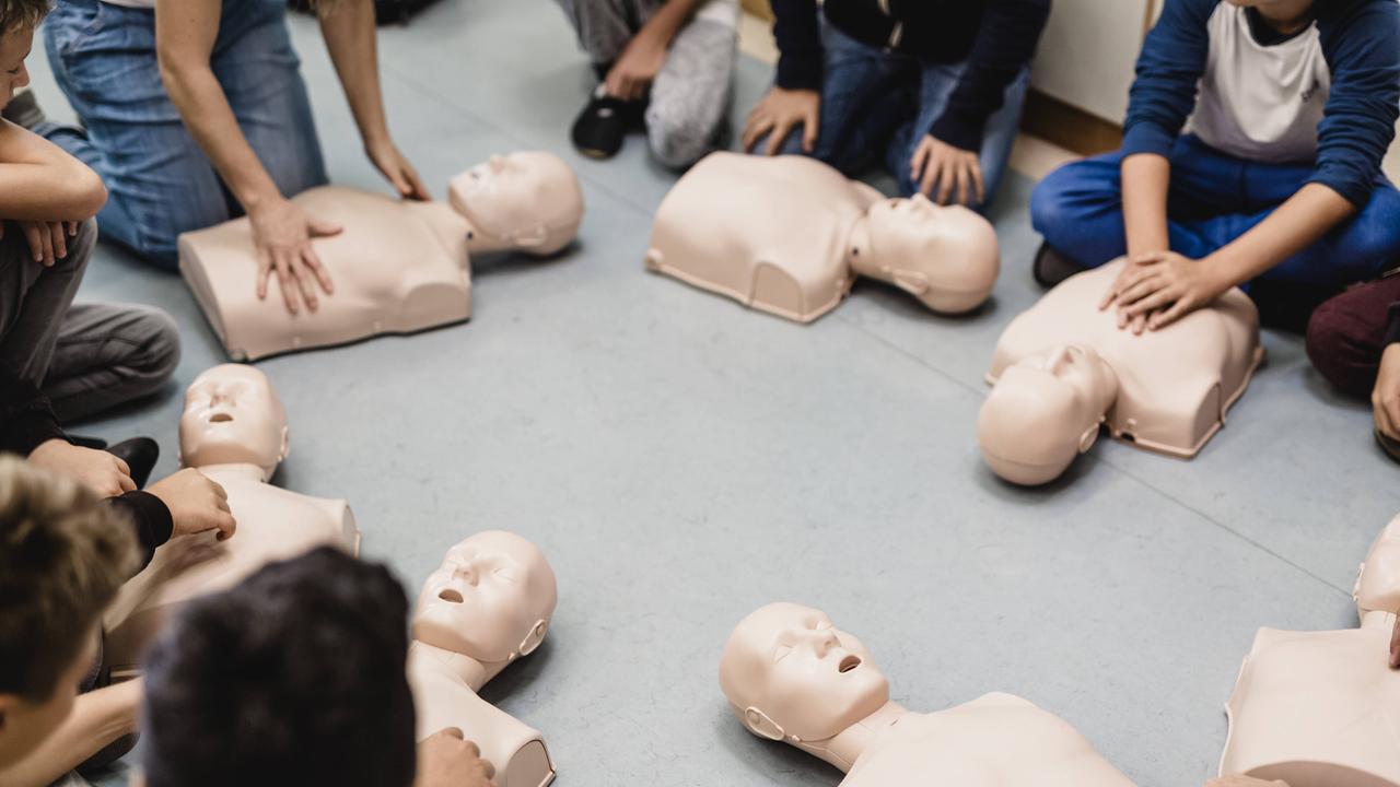 Mehrere Menschen sitzen im Kreis und üben die Reanimation an Plasikpuppen, die vor ihnen auf dem Boden liegen. 
