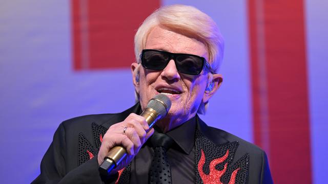 Das Foto zeigt den Sänger Heino mit einer schwarzen Sonnen-Brille. Er singt in ein Mikrofon. 