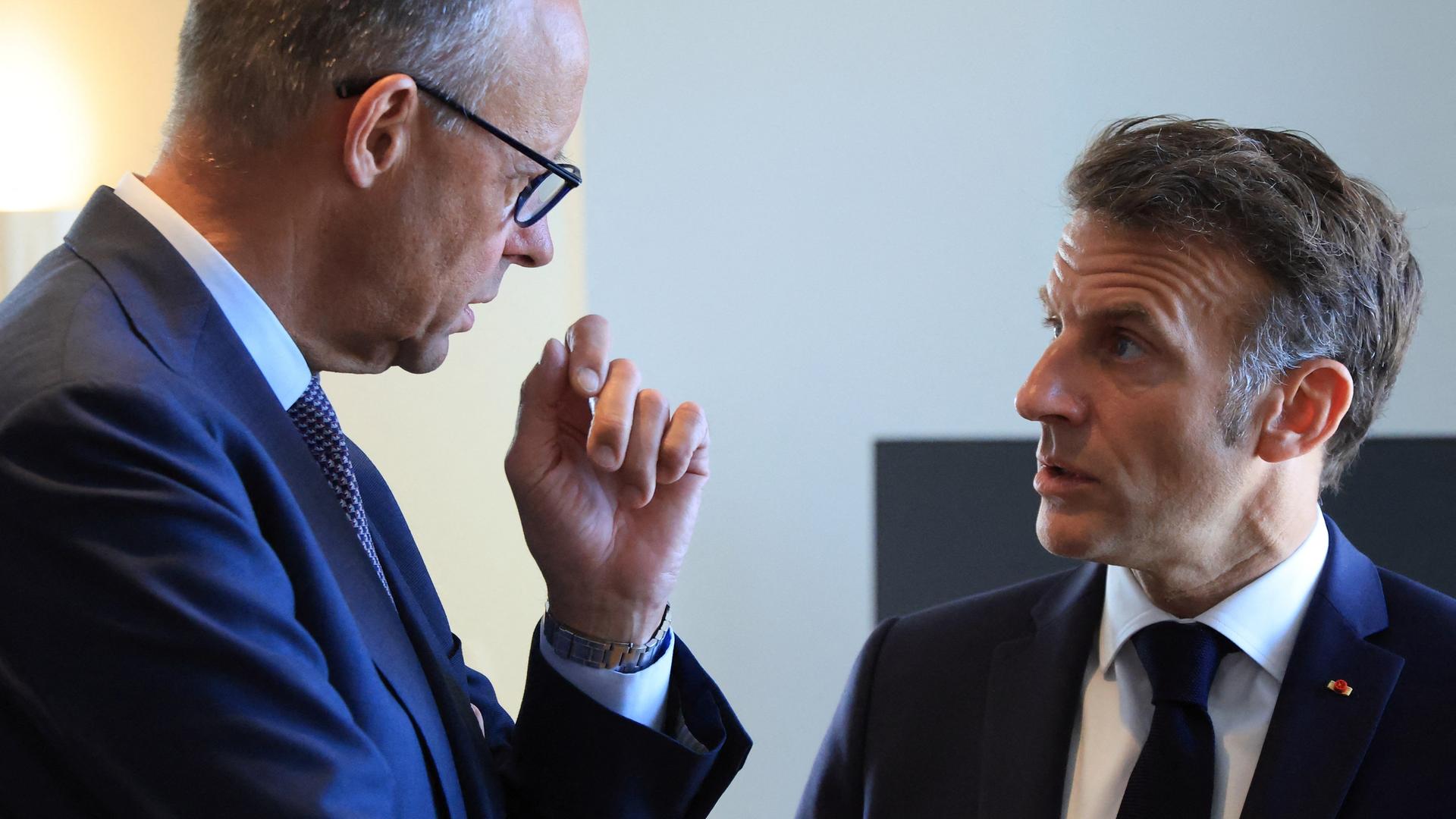Bundeskanzler Merz und Frankreichs Präsident Macron stehen sich gegenüber und sprechen vertraulich miteinander.
